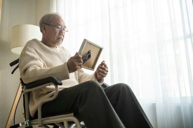 An elderly man in a wheelchair solemnly looking at a framed photograph, illustrating the personal nature of grief and the impossibility of comparing our individual experiences of loss.