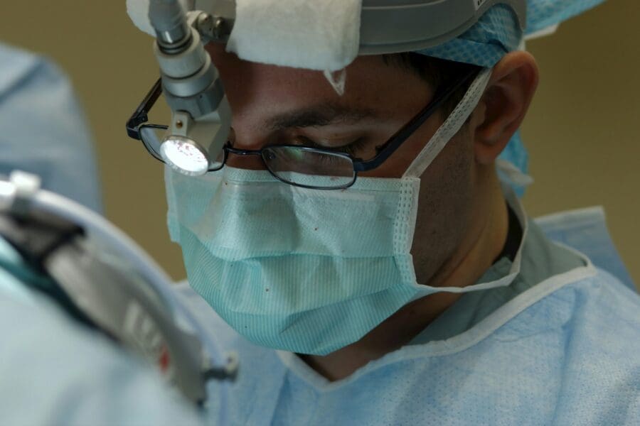 A focused medical student wearing surgical scrubs, a mask, and loupes during a procedure, embodying the theme of 'Empathy behind the Mask: Personal Stories of Grief from My Experience as a Medical Student.'