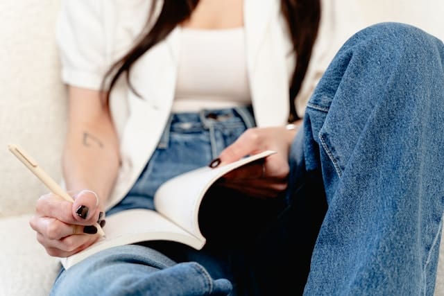 A person seated with legs crossed, writing thoughtfully in a journal, embodying the practice of journaling through grief as a means of processing emotions and finding solace.