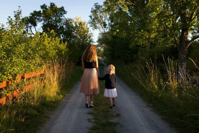 A mother and her daughter walk hand in hand along a unpaved road. Symbolizes connection and future loss.