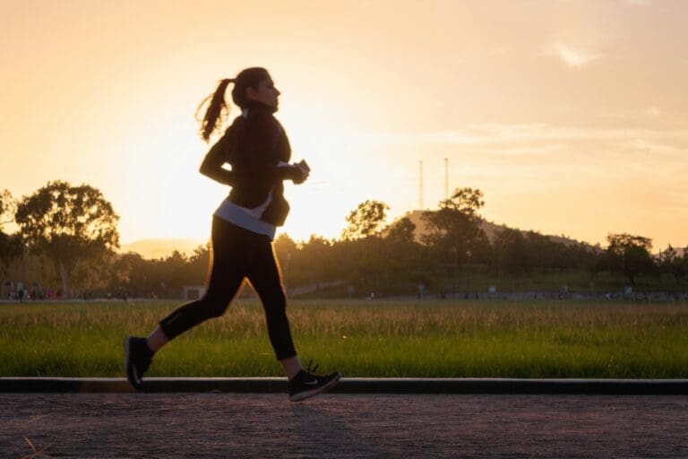 A woman jogging at sunset on a park pathway, embodying self-care and resilience as she navigates through personal grief, with the backdrop of a tranquil natural setting reinforcing the theme of healing and perseverance.